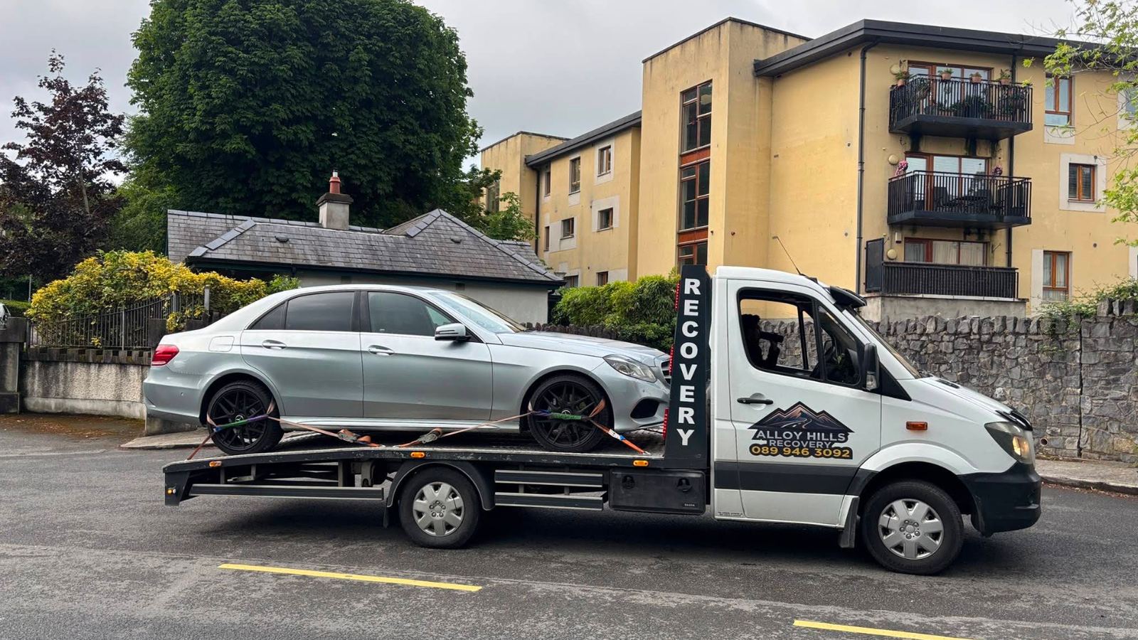 Alloy Hills Recovery flatbed recovery truck carrying a car at dusk
